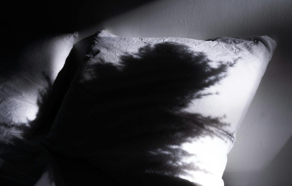 Black and white shadow cast on a wrinkled pillow creating a dramatic scene.