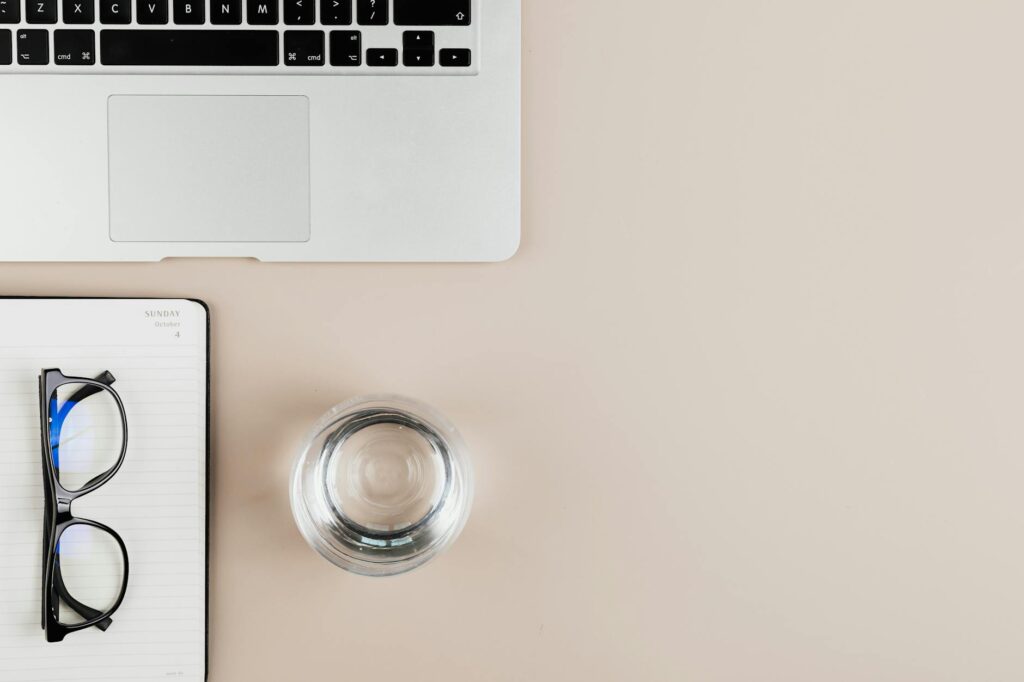How Can I Manage ADHD-Related Executive Dysfunction in Daily Life? 6 Overhead view of a clean workspace with a laptop, notebook, eyeglasses, and a glass of water.