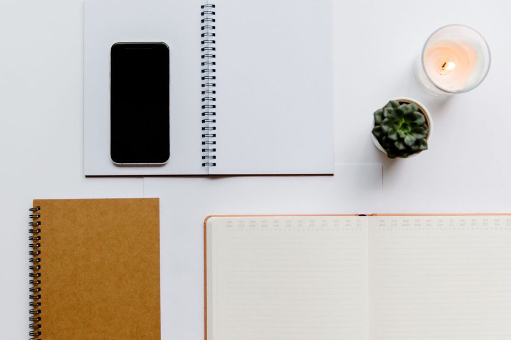 How Can I Manage ADHD-Related Time Blindness to Improve Daily Life? 4 Aerial view of a minimalist office setup featuring notebooks, a smartphone, candle, and succulent on a white background.