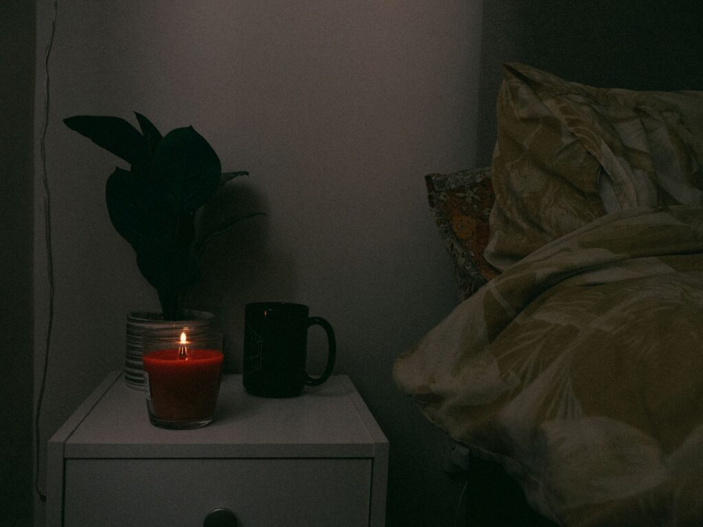 How Can I Manage ADHD-Related Impulsivity and Improve Self-Control? 5 A cozy nightstand scene with a candle, mug, and plant beside a bed, creating a warm atmosphere.