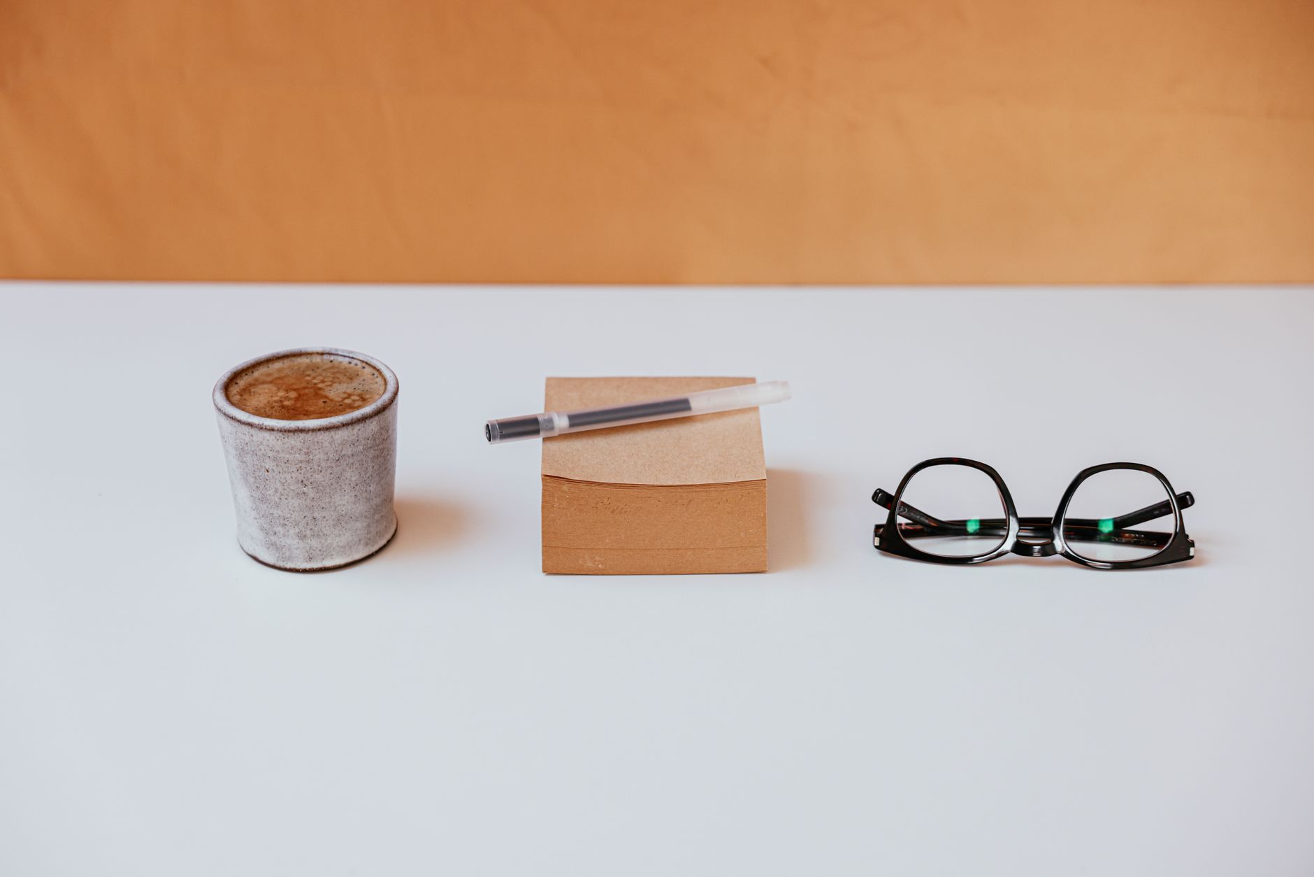 A minimalist workspace with a coffee cup, sticky notes, and eyeglasses on a white desk.