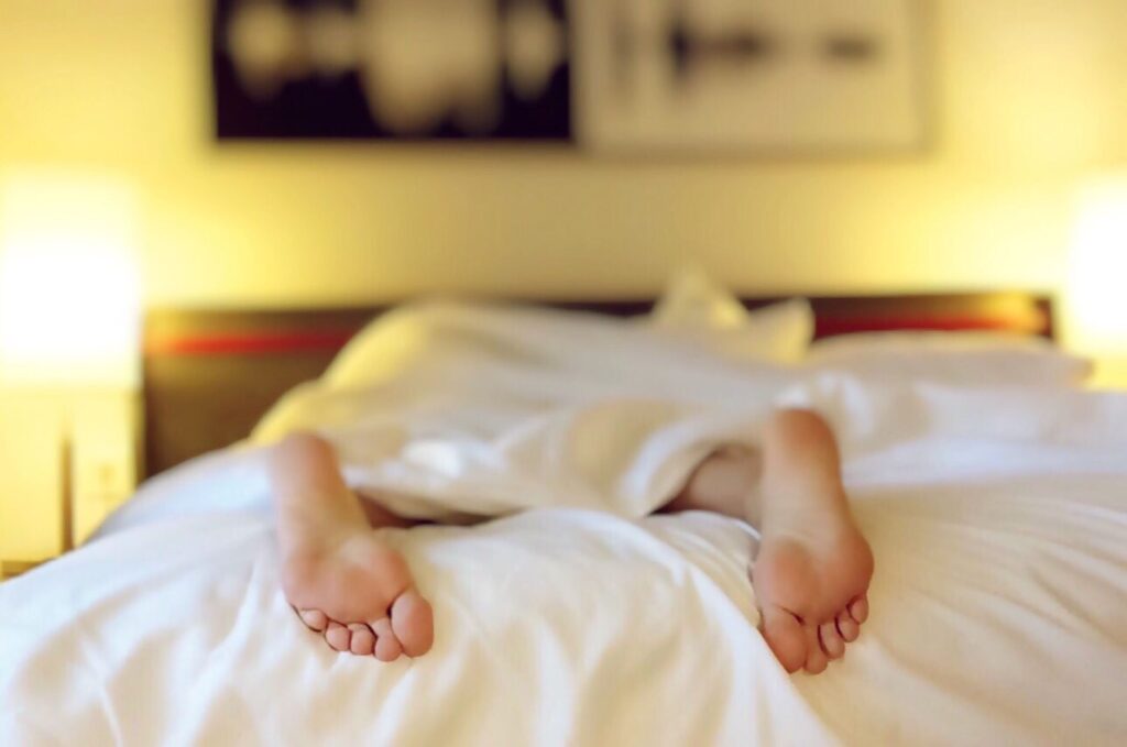 A person relaxing on a bed with feet under white sheets, conveying serenity.